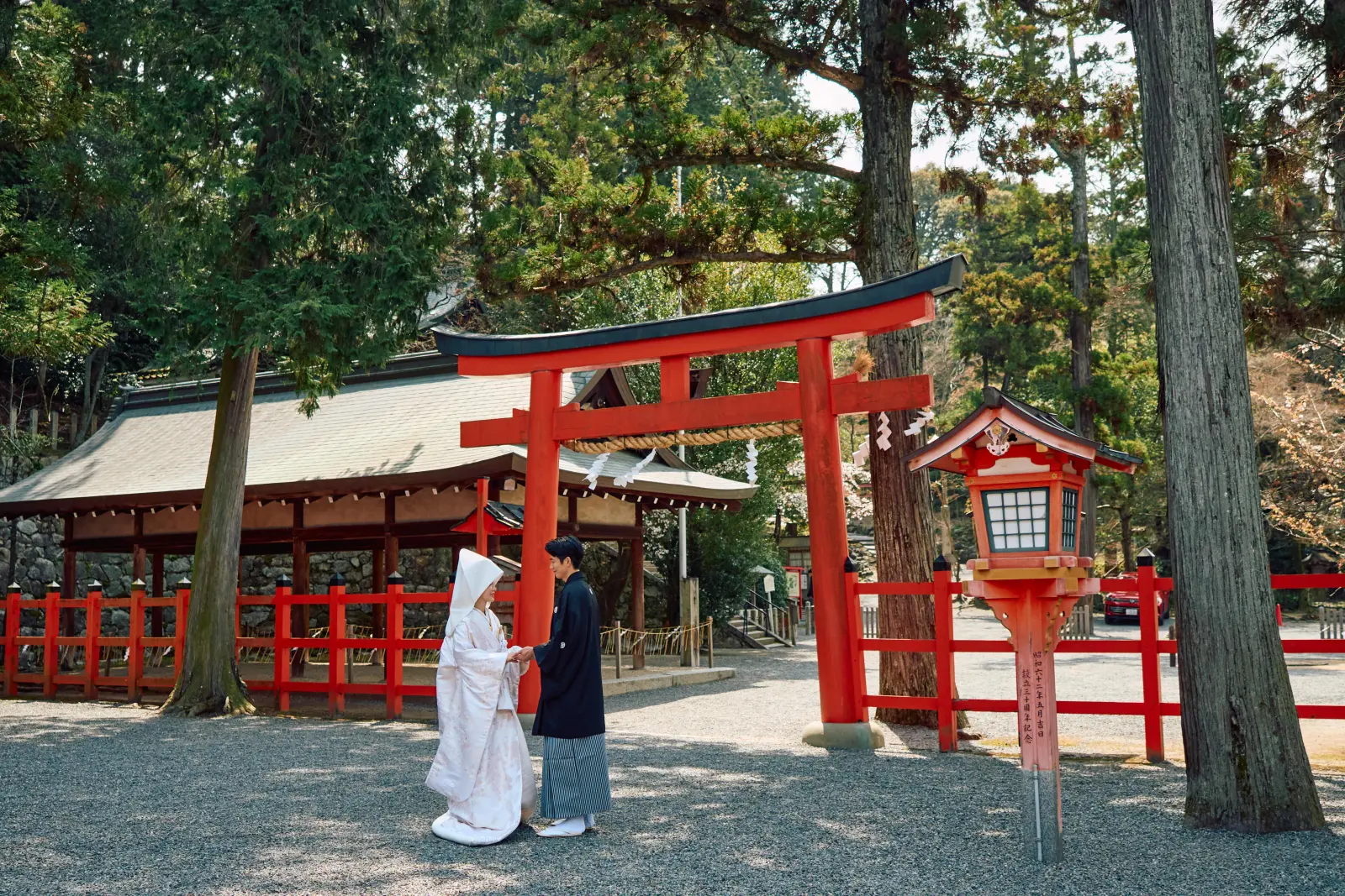 神社の鳥居の前で手を取り合う白無垢と紋付袴のおふたり